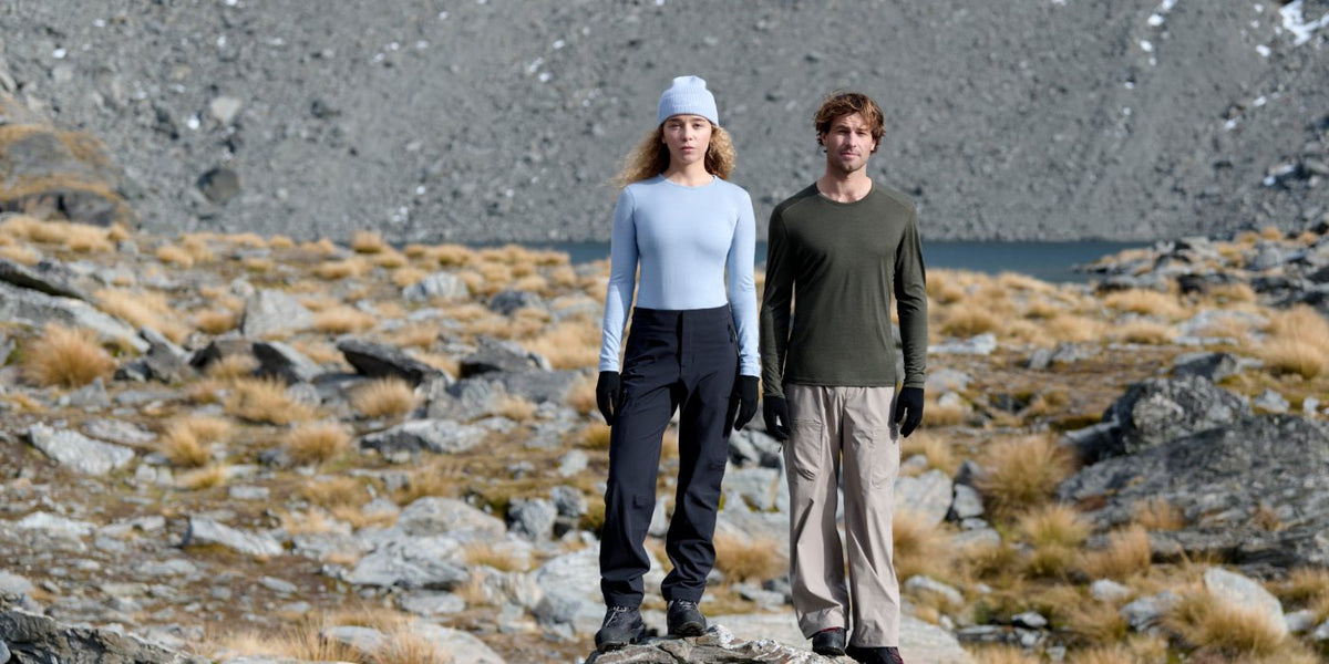 Two hikers in Icebreaker 200 Oasis merino base layers standing on a rocky ridge above a mountain lake